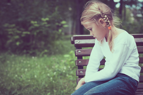Sad little girl sitting on bench.