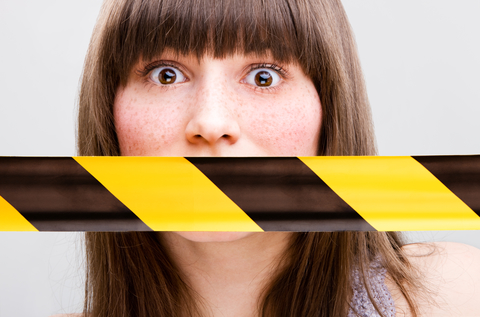 Woman's face with caution tape in front of her mouth and across the image.
