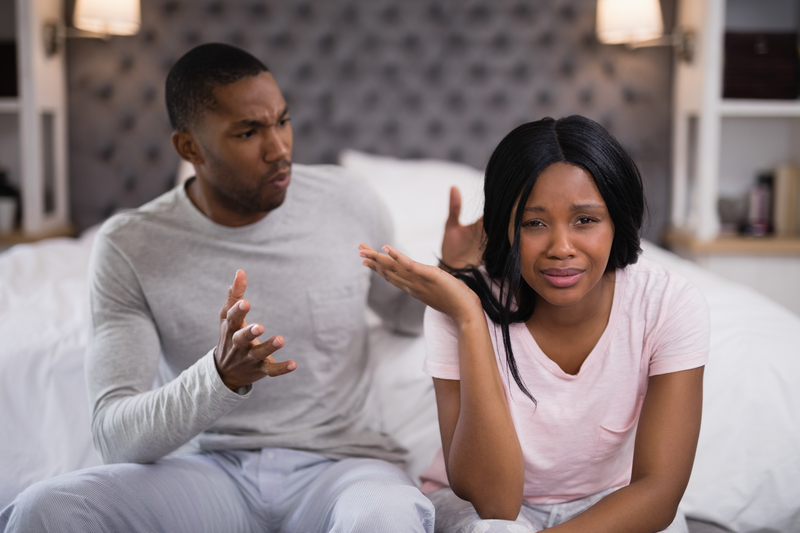 Young couple arguing, sitting on edge of bed.