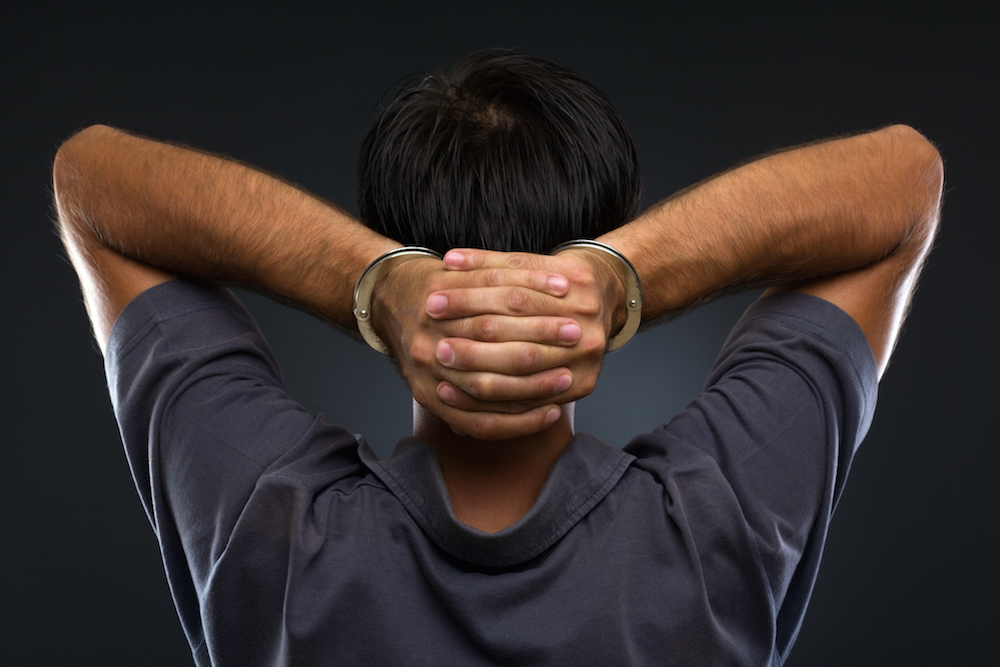 man with handcuffed hands behind his head
