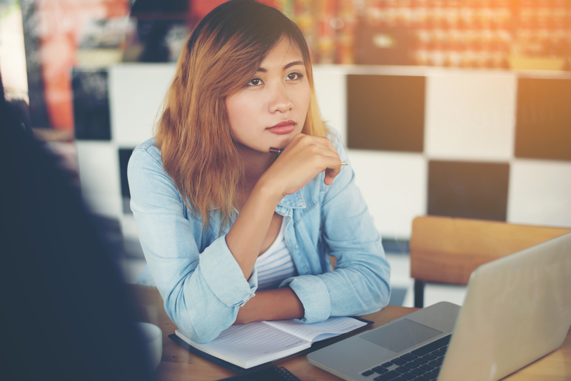 Woman gazes into the distance as she sits at table with laptop computer.
