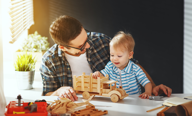 Father and toddler son building a model truck with popsicle sticks.