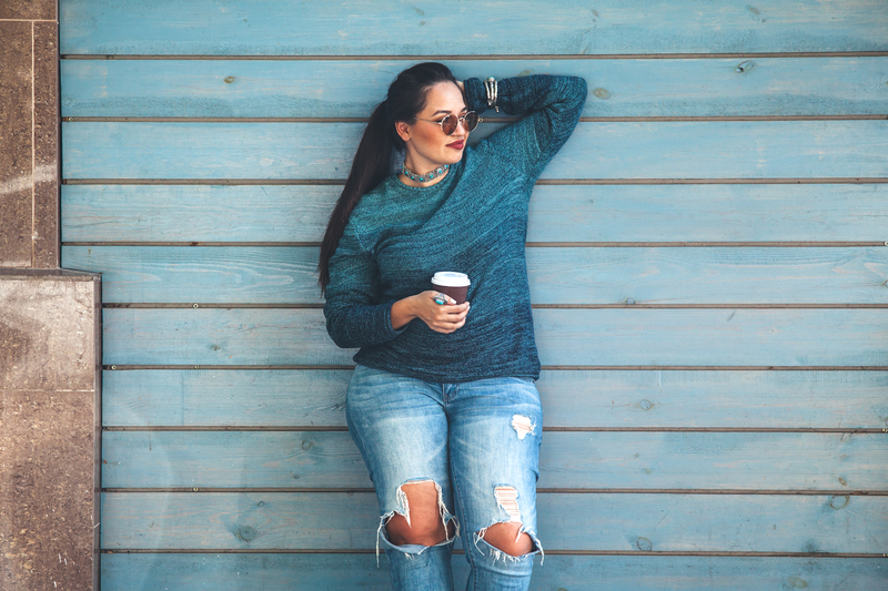 Woman standing against a wall with drink in hand, happy.