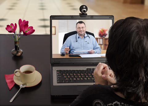 A woman faces a computer screen where a doctor is looking out at her.