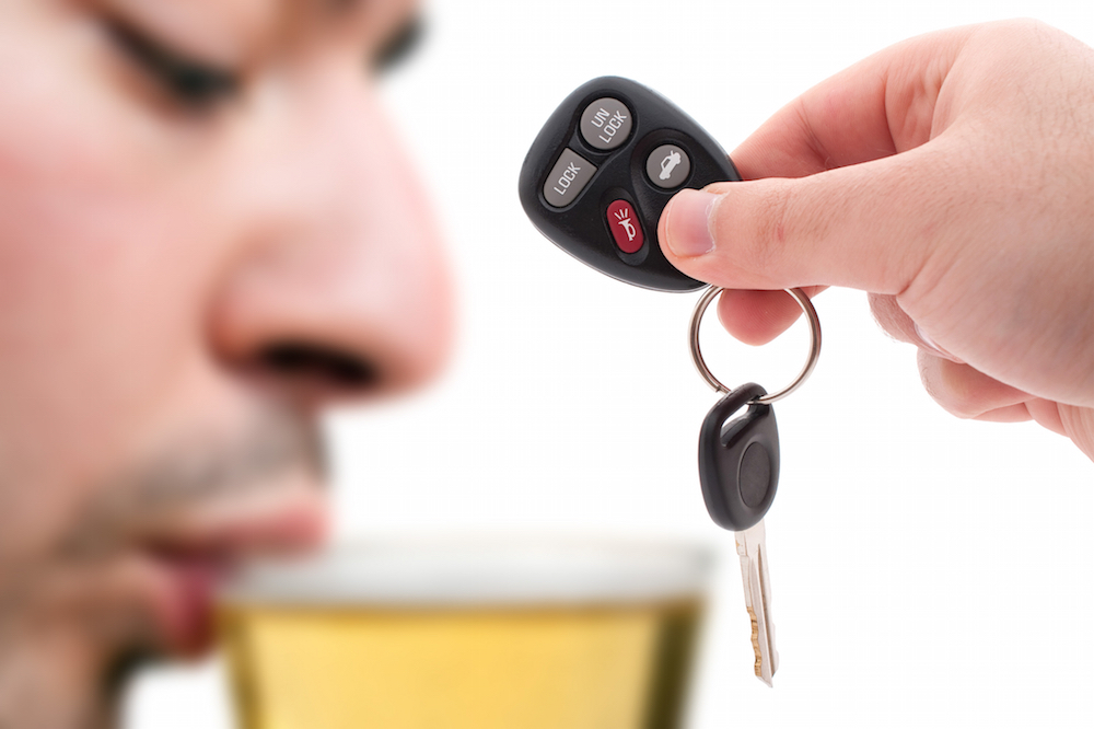 man sipping a beer while a hand in the foreground holds a key fob.