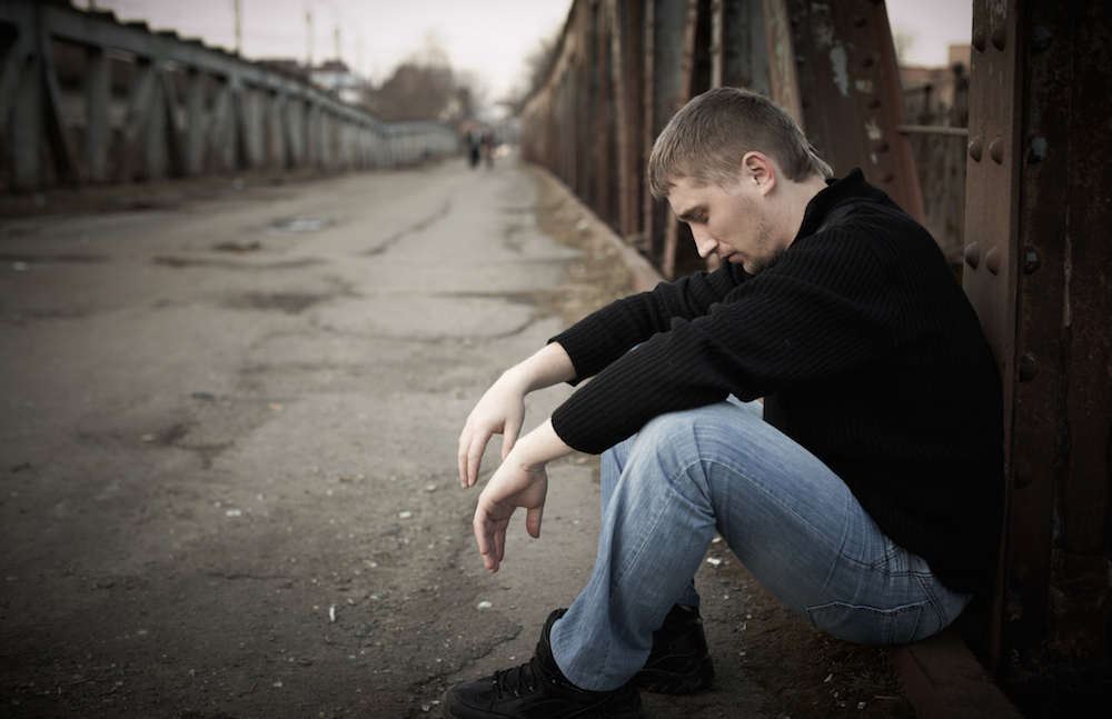 pensive young man sitting down on the street