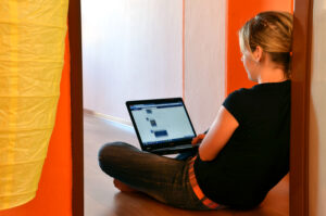 Woman sits on floor browsing Facebook on her laptop.