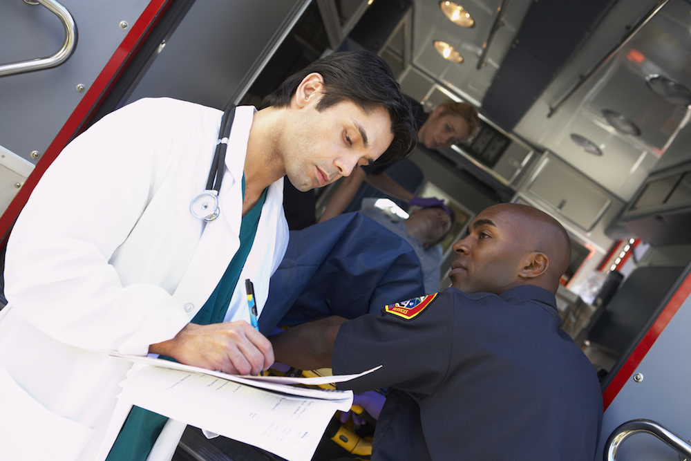 Hospital doctor taking notes as paramedics arrive with patient