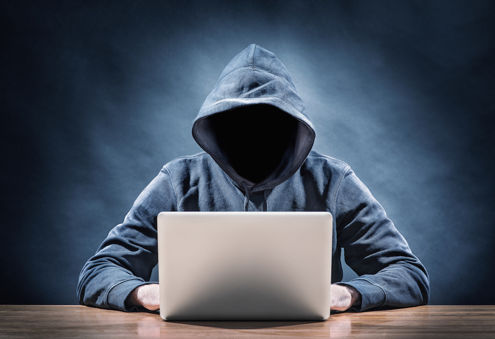 mysterious person with hoodie typing on laptop