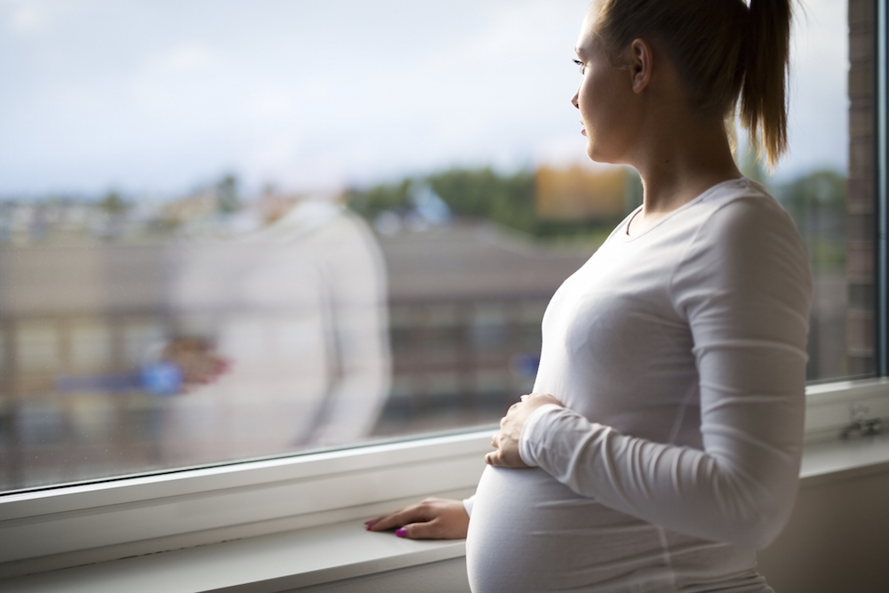 pregnant woman looking out the window of home