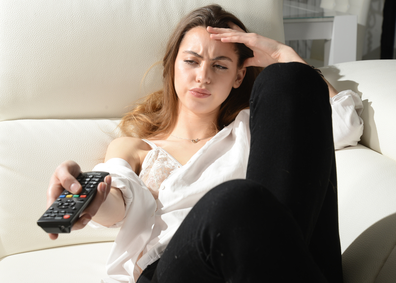 Woman holding TV remote with confused expression.