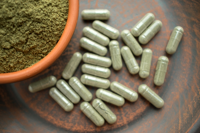 A bowl of green powder next to green capsules (kratom)