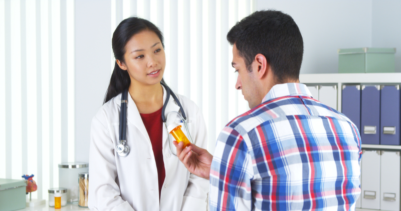 A doctor looks at her male patient who is holding a prescription pill bottle.