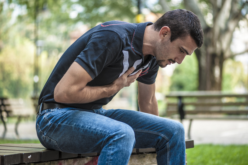 Man sits on bench in park, clutching heart.