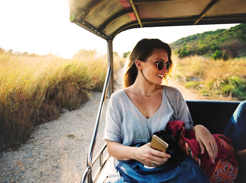 Smiling woman in back of jeep, traveling through fields or bush.