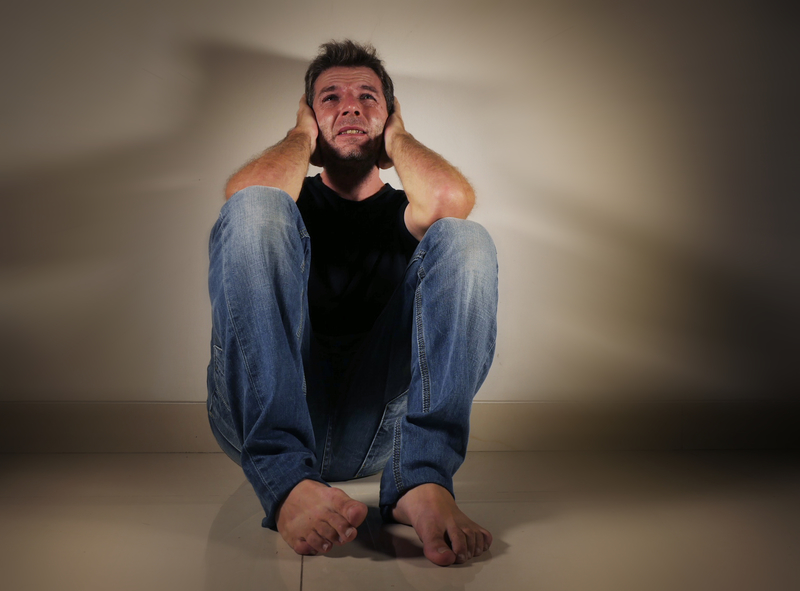 Young man sitting on the floor, hands at sides of head. Looks anguished.