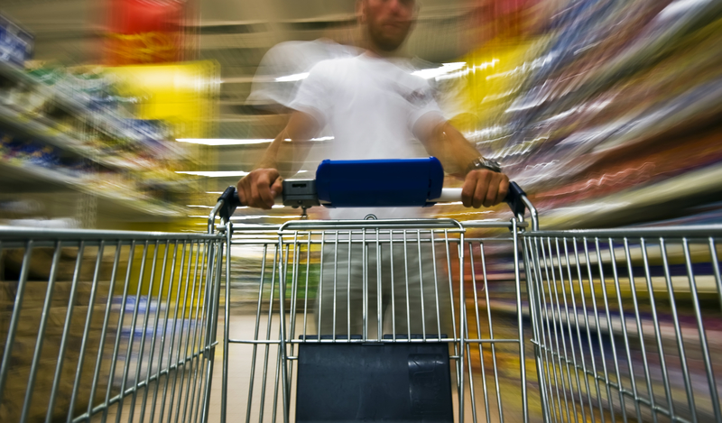 An empty shopping cart being pushed by a blurry person in a blurry supermarket.