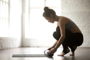 woman crouches while unrolling her yoga mat
