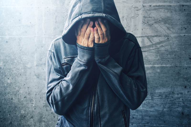 Man in hoodie with hands covering his face.