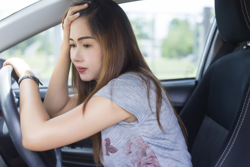 Woman in driver's seat, resting arm on steering wheel, looks sad or stressed.
