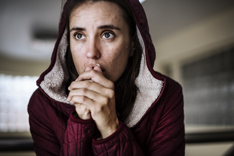 Woman in hooded jacket with hands at mouth as in prayer