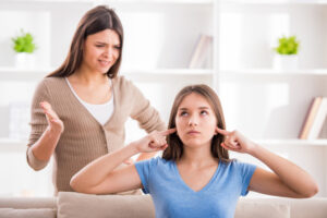 Mother trying to talk to teen who has fingers stuck in her ears.
