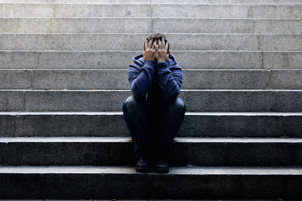 sad man sitting on stairs with hands covering his face