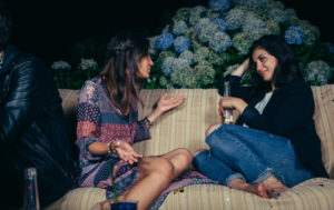Two women talking on a couch, one has a drink in hand. How to talk about addiction.