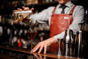 Close up of bartender pouring bright red alcohol cocktail into the glass