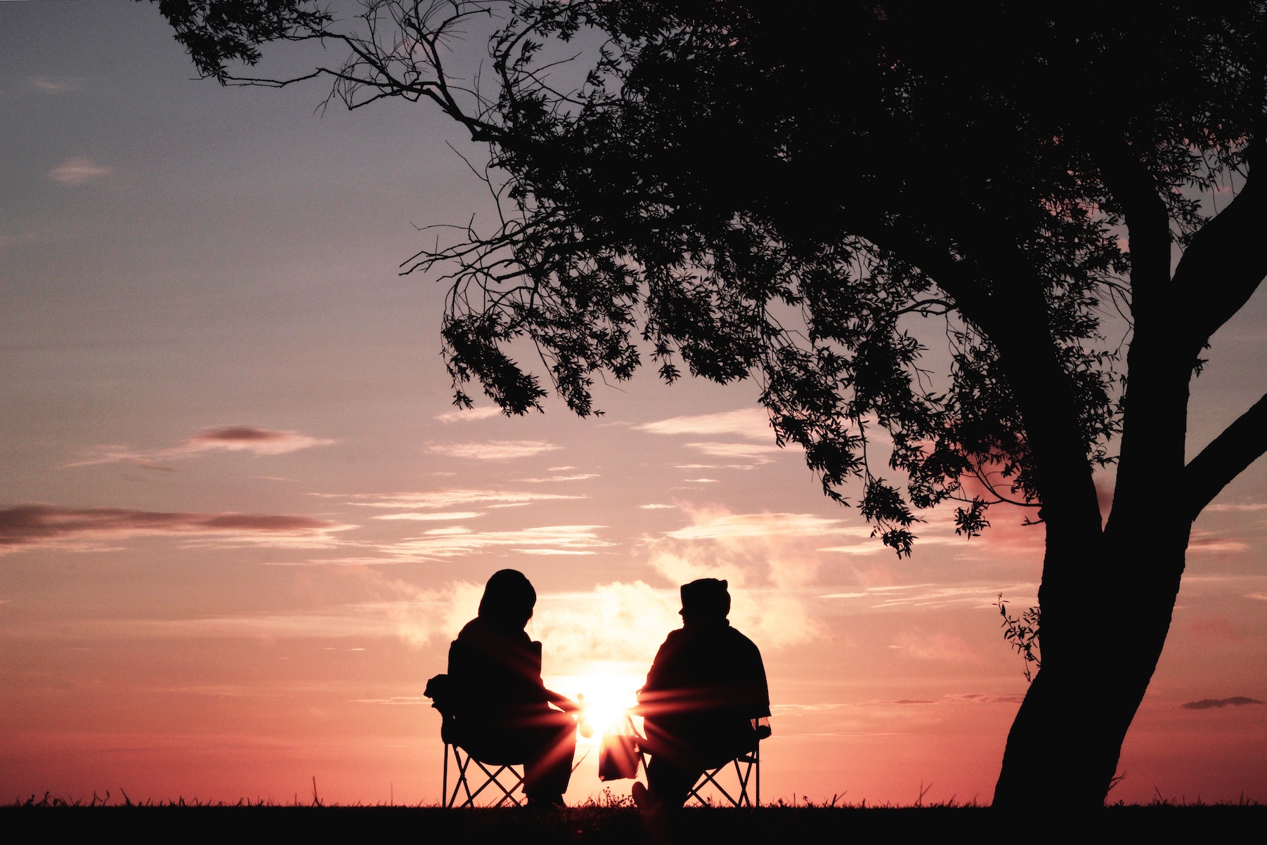 Two people silhouetted by sunset, sitting and talking, father and daughter discuss addiction recovery