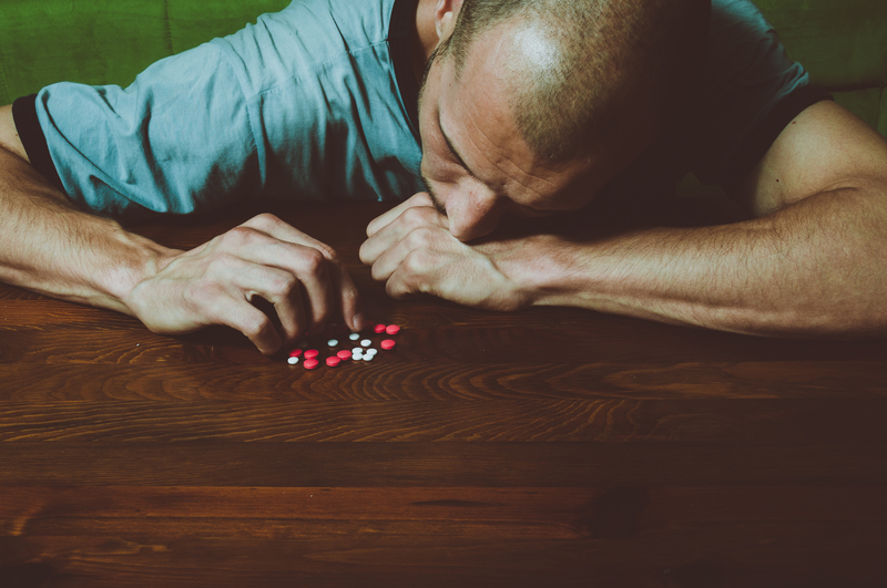 Man with head on table with synthetic drugs, pills