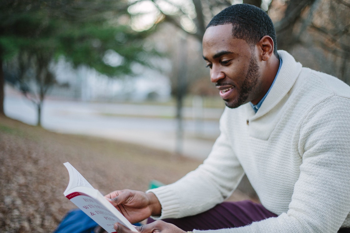 Man sitting, smiling, reading a book, self-discipline in sobriety
