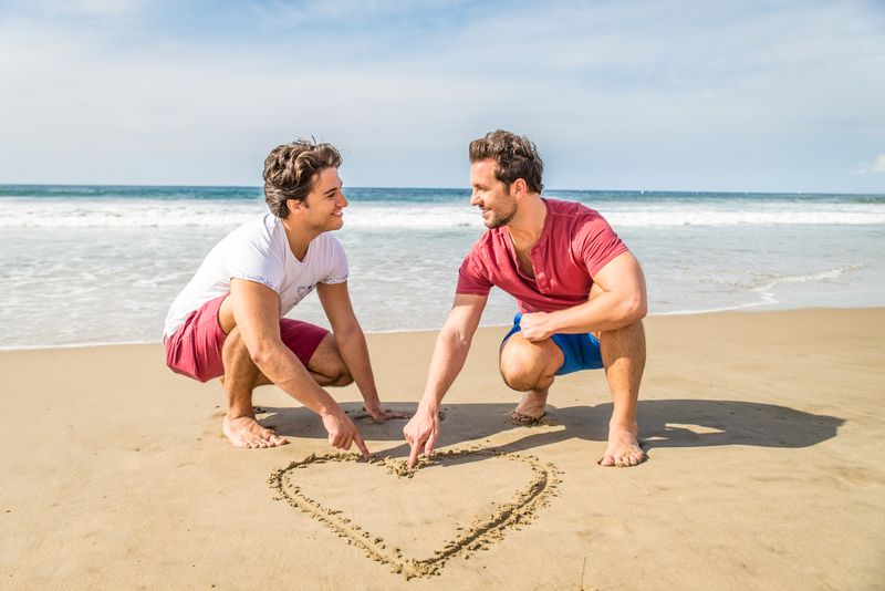 two gay men on a sober date at the beach drawing a heart in the sand