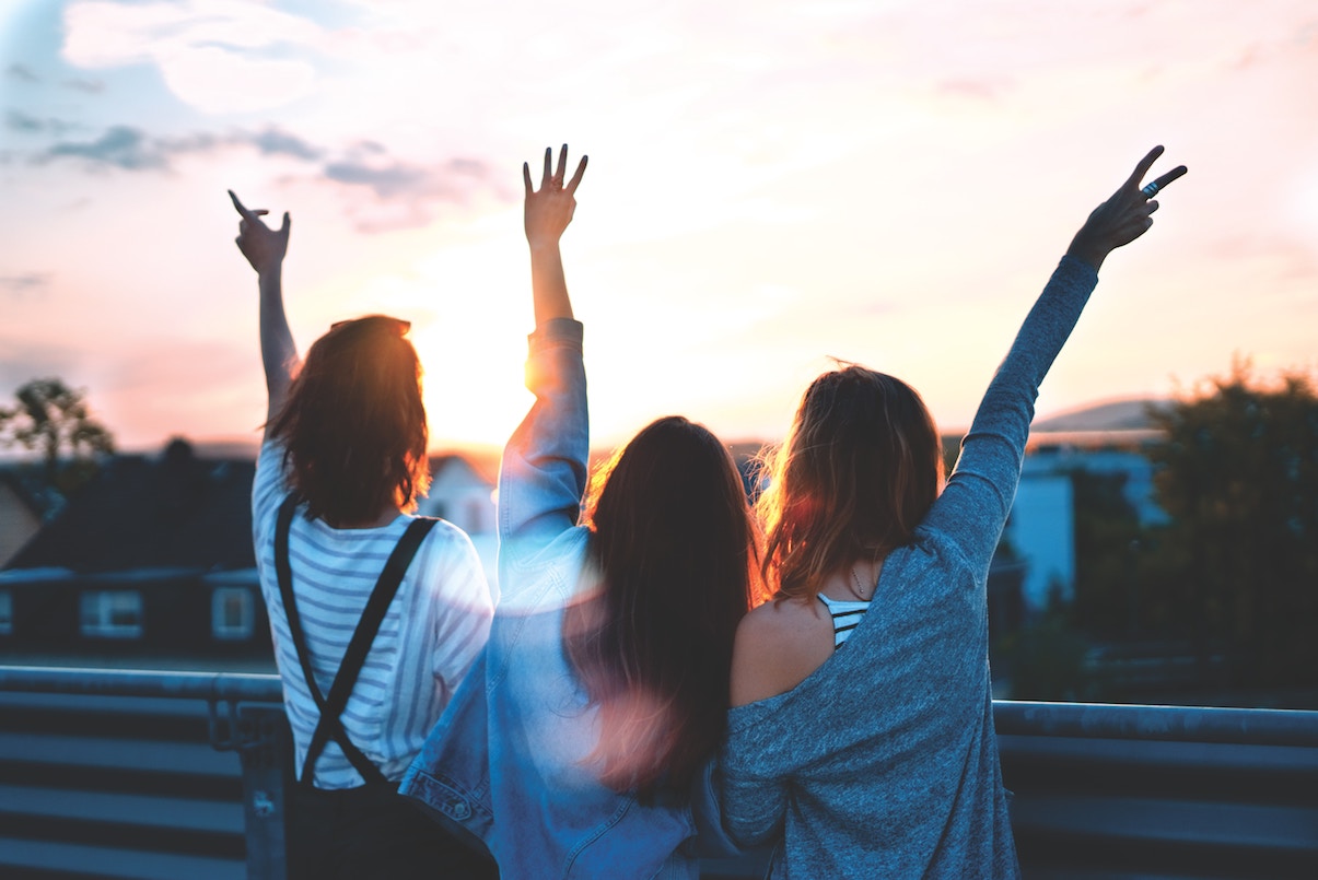Group of women with arms up in the air in joy, facing sunset