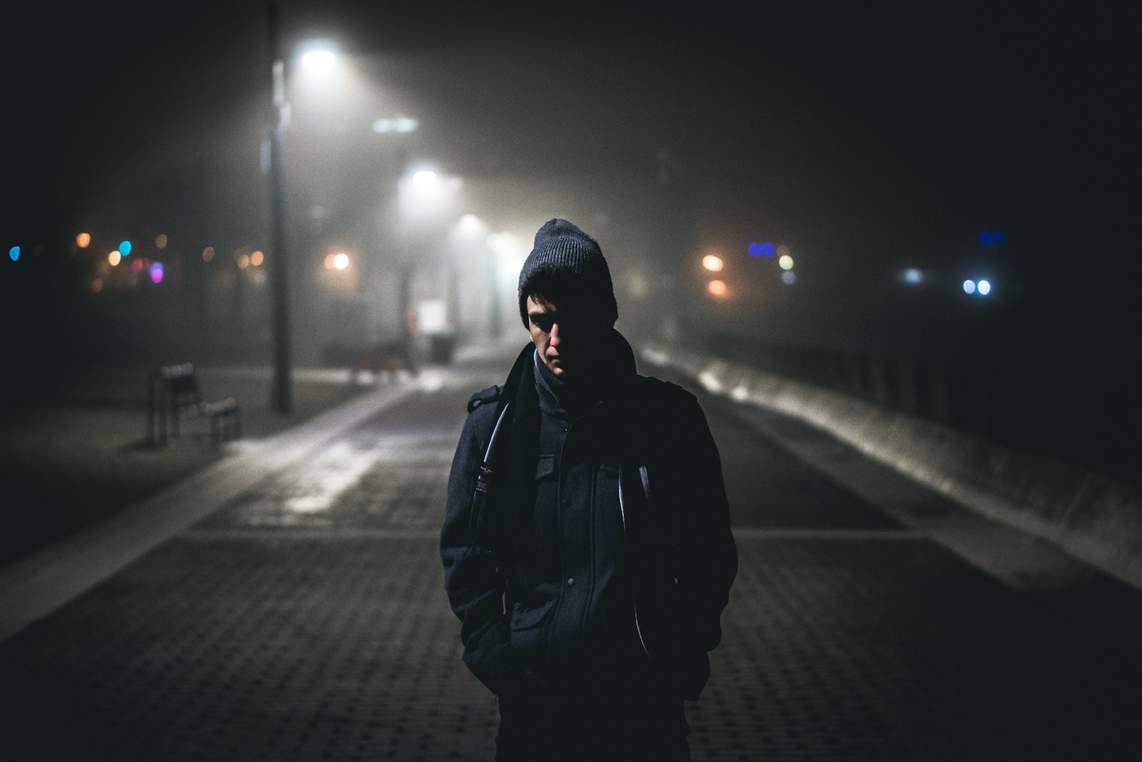 Man alone on a street in hooded jacket, looking down.