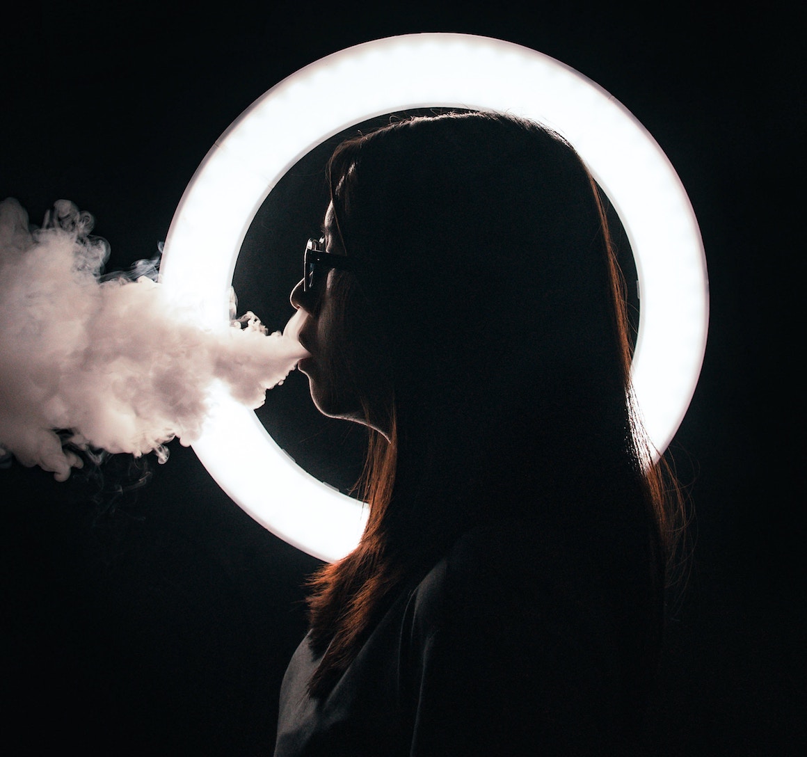 Face in silhouette in circle exhaling smoke or vapor, person vaping