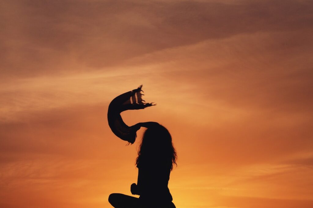 On Ascension: Finding the Courage to Heal and Grow Person silhouetted against sunset, waving scarf in the air.