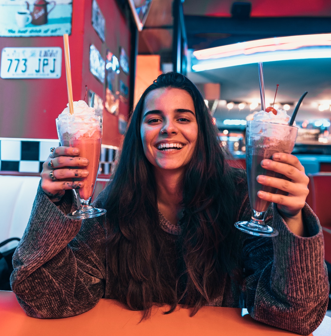 Woman holding two milkshakes in restaurant and smiling