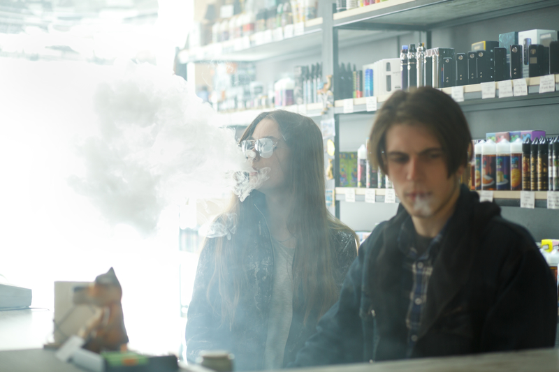 Vape teenagers. Young cute girl in sunglasses and young handsome guy smoke an electronic cigarettes in the vape bar. Bad habit that is harmful to health. Vaping activity.