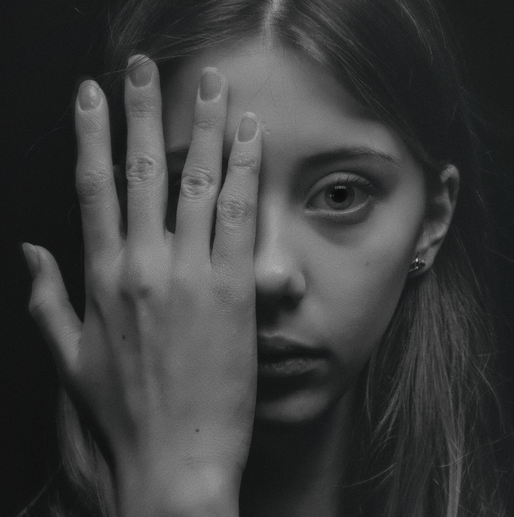 black and white image of a girl's face with her hand covering half of it.