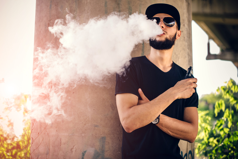 hipster with dark cap and sungleasses blowing vape cloud