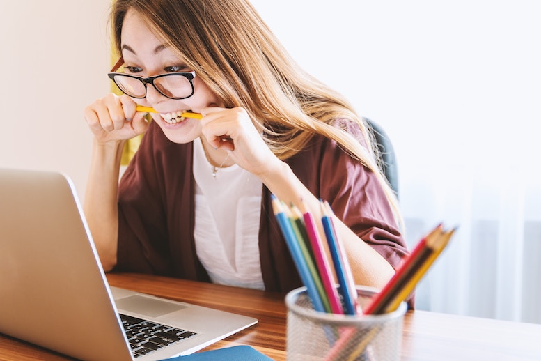 Young woman sitting in front of laptop bites a pencil in frustration.
