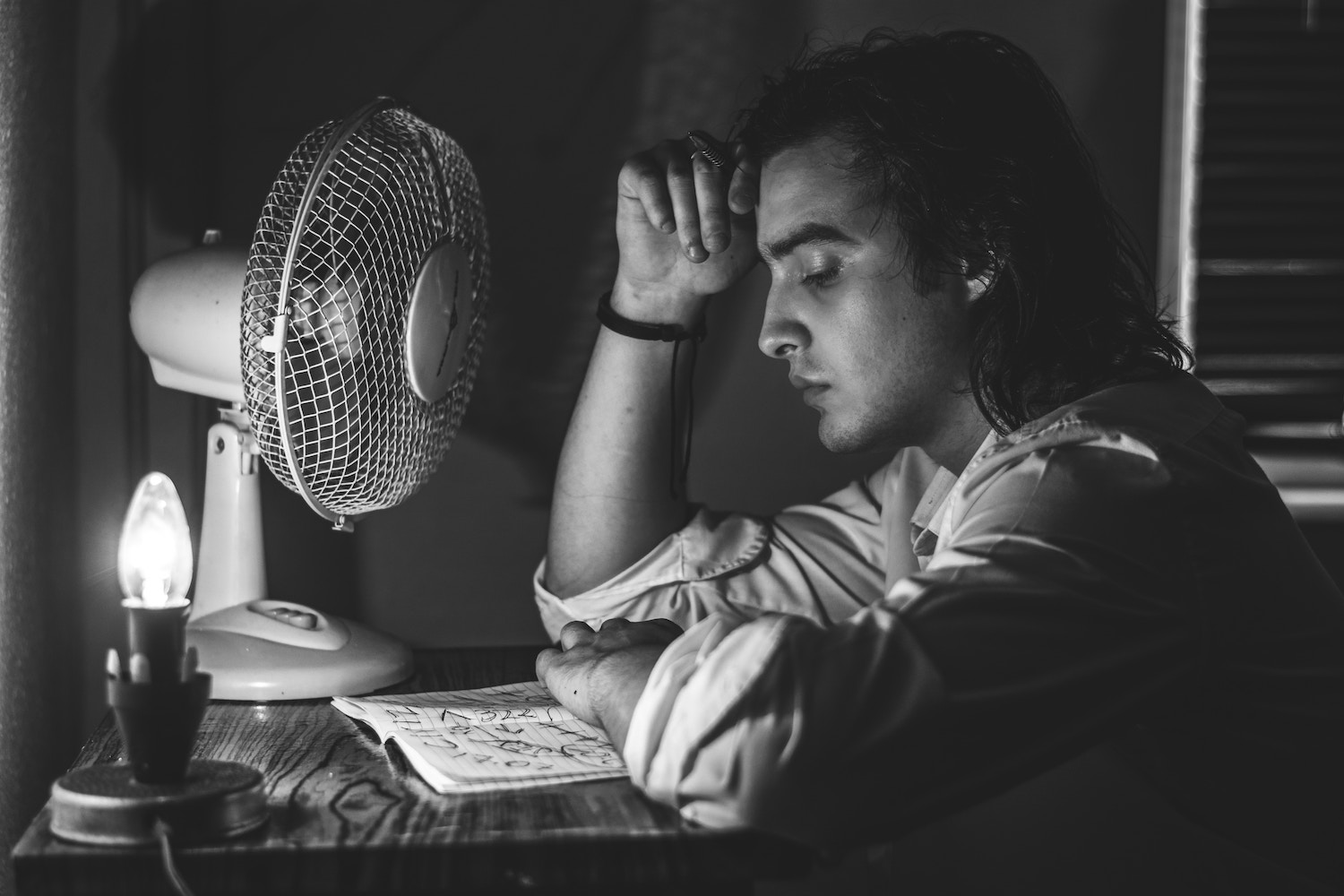 black and white pic of man with notebook and pen, thoughtful, writing