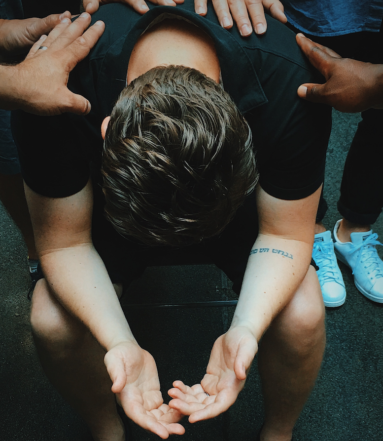 young man, head bowed, receiving laying-on-of-hands by group