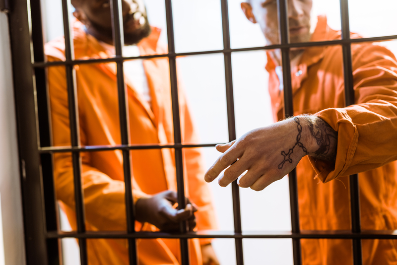Two men in orange jumpsuits behind bars