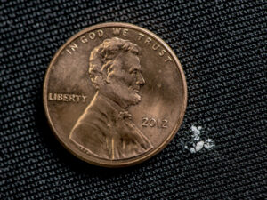 tiny pieces of fentanyl next to a U.S. penny (.1 cent) for scale.