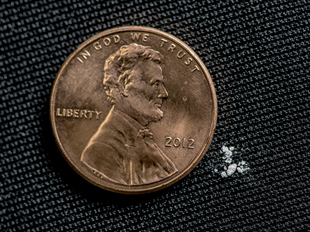 tiny pieces of fentanyl next to a U.S. penny (.1 cent) for scale.