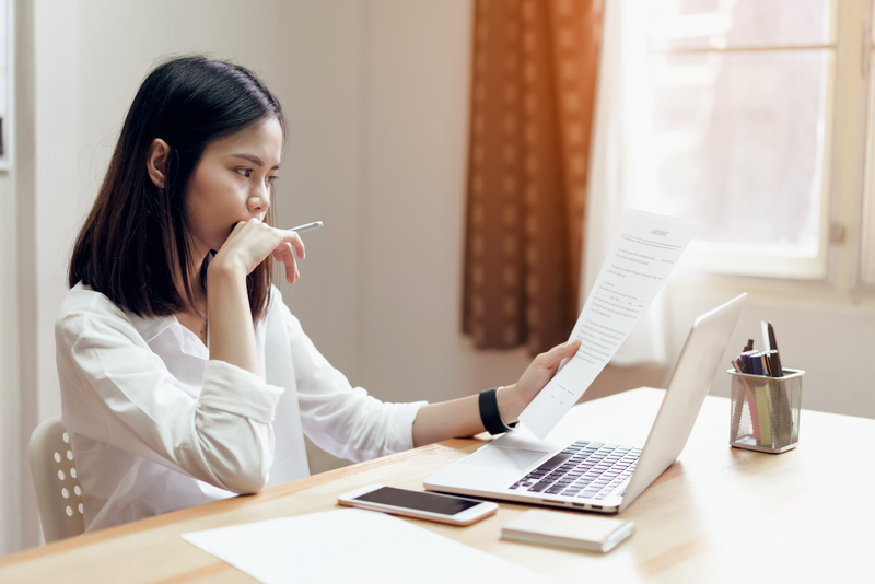 Woman at desk looking at paper and computer screen, budgeting