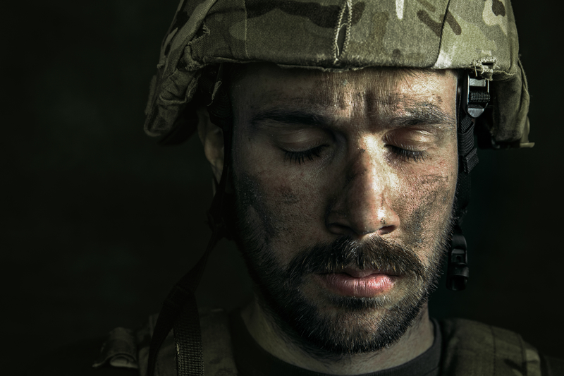 Close-up of man's face in military helmet, eyes down, sad.