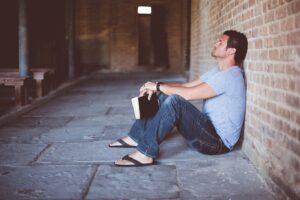 Man sitting against brick wall, book or bible in hand
